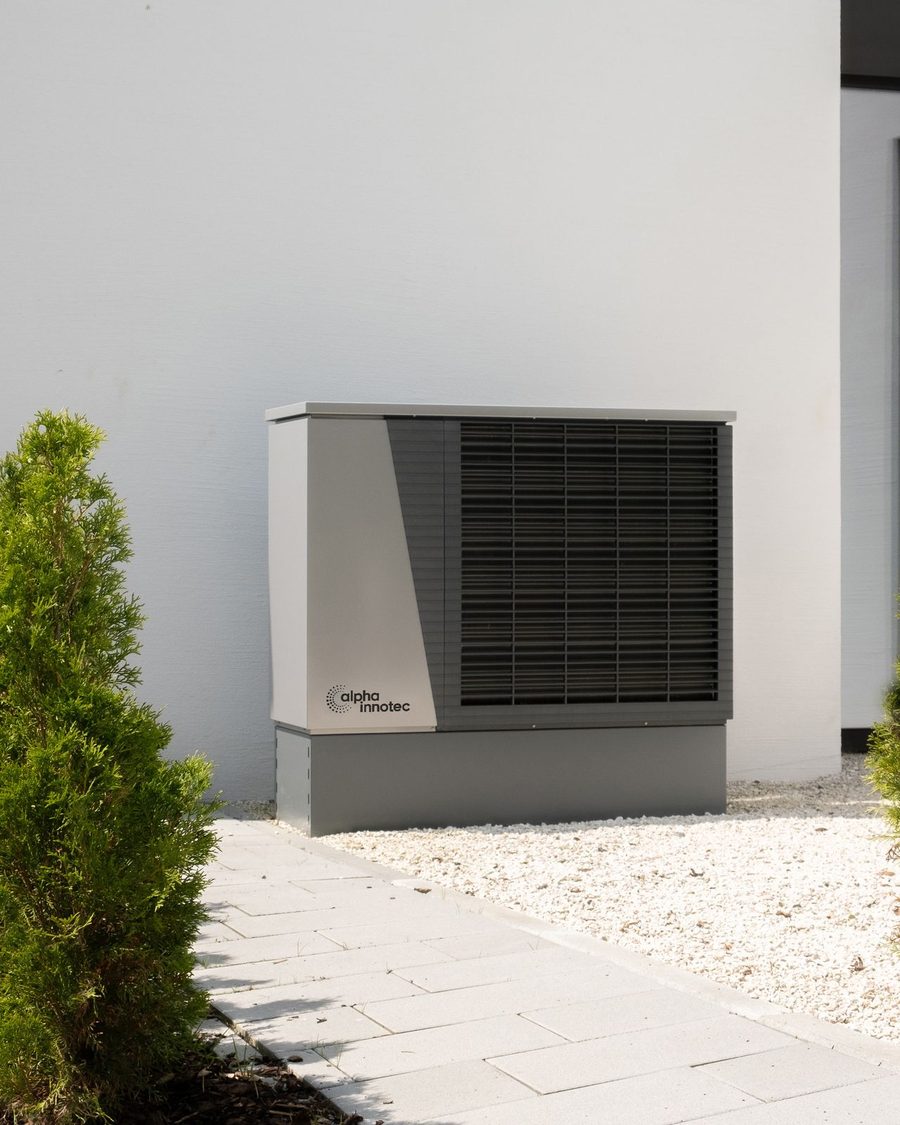 A new outdoor unit on a pad beside a white stucco wall with gravel and shrubs