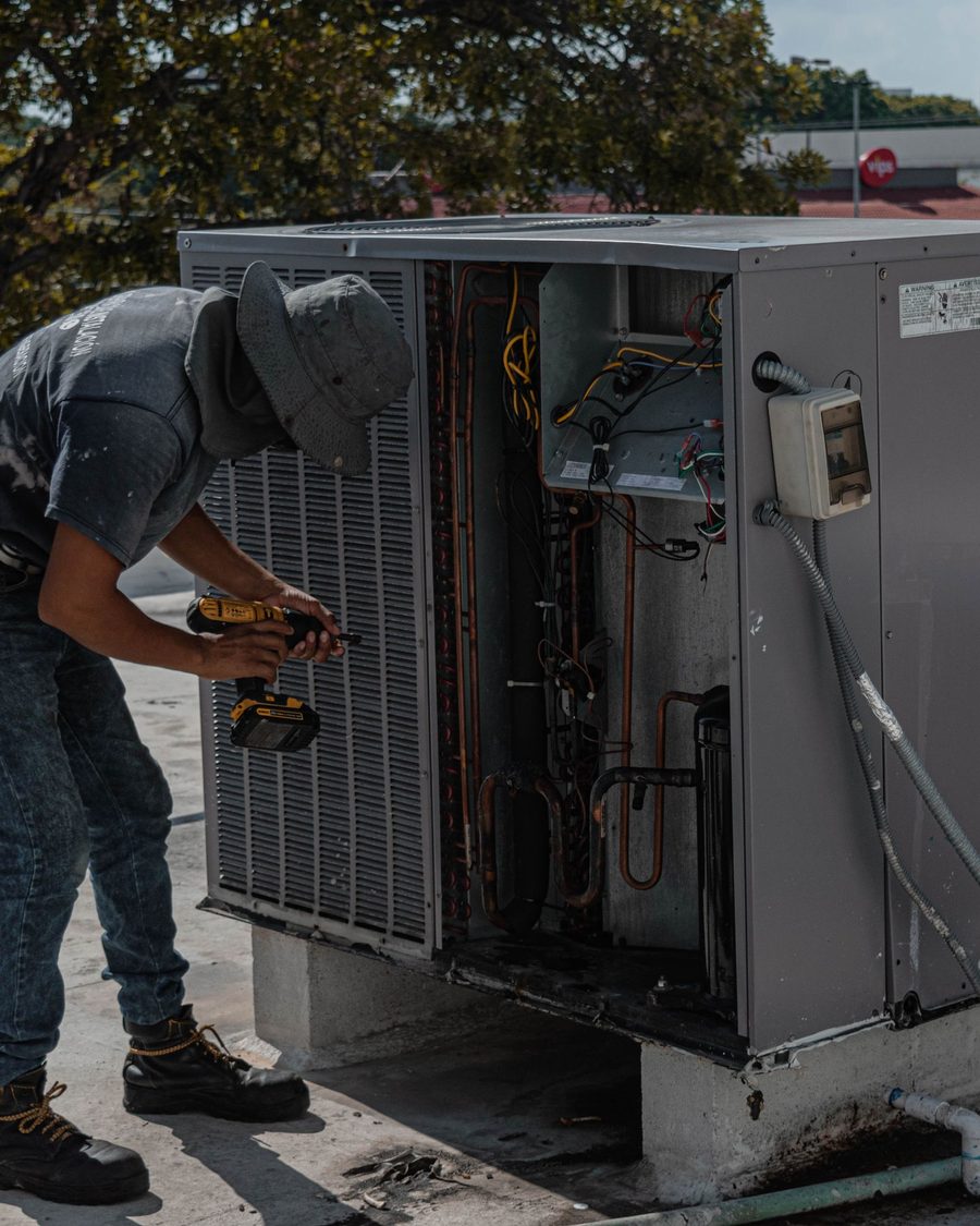 A worker with a drill at an open rooftop air conditioning unit