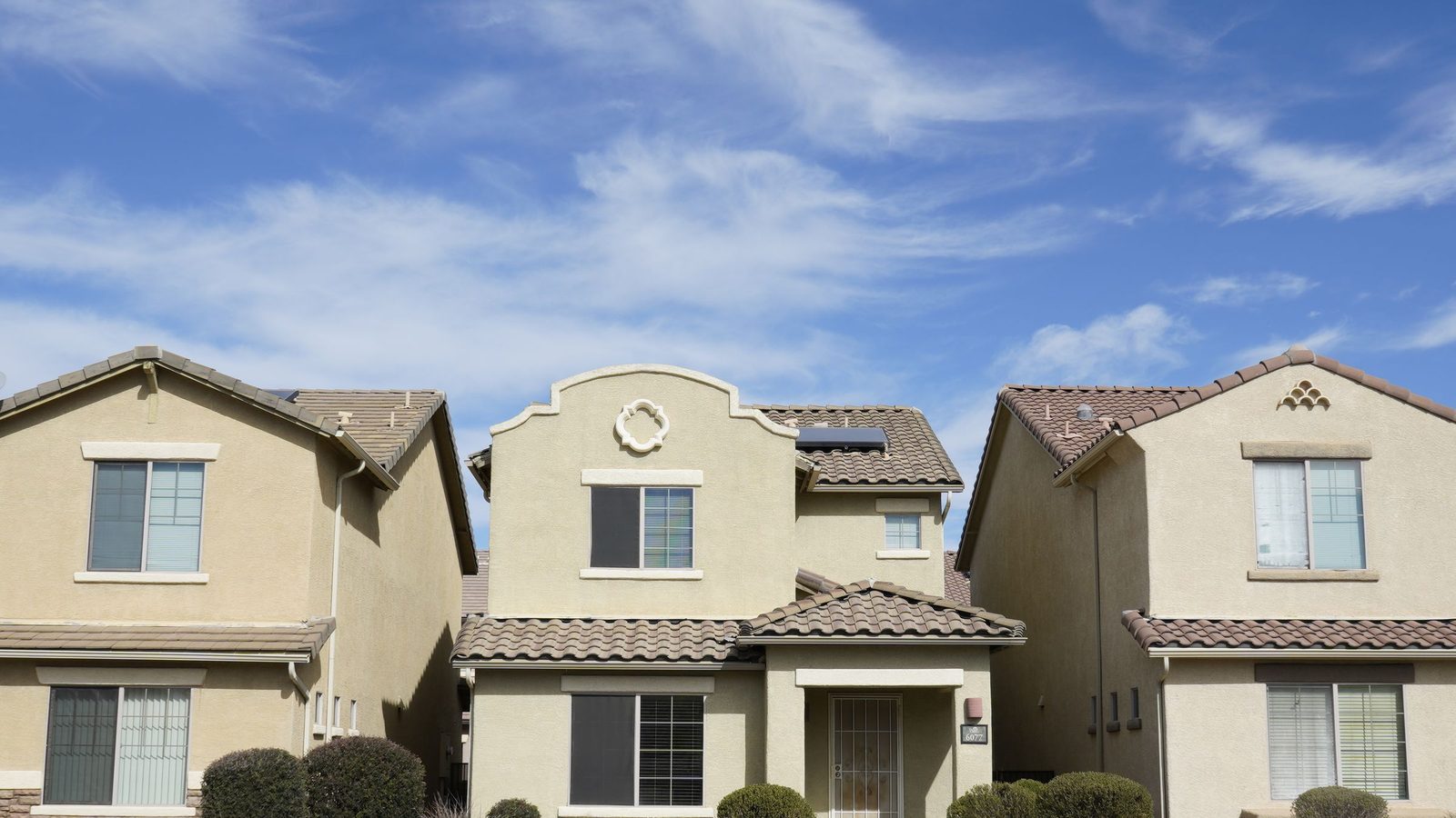 Three stucco houses with tile roofs on a suburban Arizona street under a clear sky